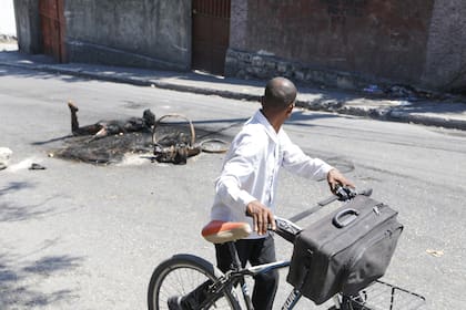 Un hombre empuja su bicicleta junto al cuerpo de una persona que fue asesinada e incendiada en Puerto Príncipe, Haití, el martes 5 de marzo de 2024.
