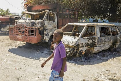 Un chico camina junto a autos carbonizados frente a una comisaría de policía incendiada por bandas armadas en Puerto Príncipe, Haití. (AP Photo/Odelyn Joseph)
