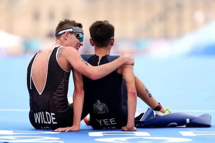 Hayden Wilde de Nueva Zelanda acaba de perder la medalla de oro en triatlón masculino, pero eso no le impide animar a su amigo, el británico Alex Yee, quien exhausto celebra en el suelo el oro conseguido.