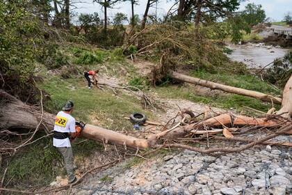 Hayley Bosworth, al fondo, y Simon Ball, a la izquierda en primer plano, cortan ramas de árboles durante labores de limpieza luego de una inundación, el lunes 7 de julio de 2025, en Center Point, Texas. (AP Foto/Ashley Landis)