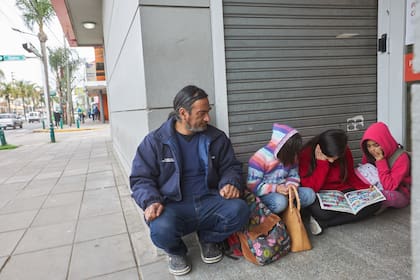 Héctor y sus tres hijas, en la puerta del banco frente al que se sientan cada tarde.