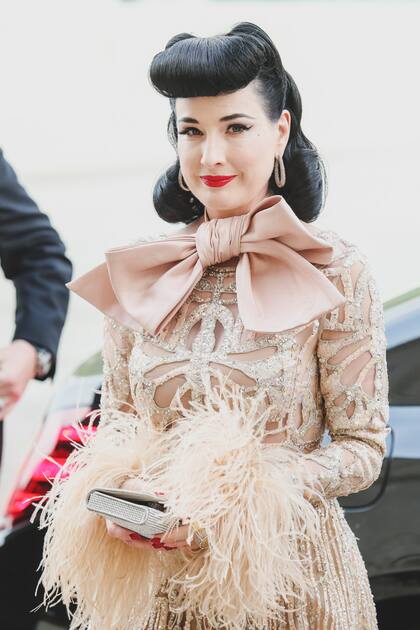 La modelo y actriz Dita von Teese eligió un traje con hilos de oro que remataba en un moño al cuello, firmado por el padre del novio.