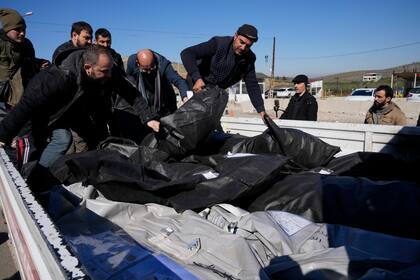 Hombres cargando cuerpos de víctimas sirias para su traslado a Siria en la localidad  de Cilvegozu, en el sur de Turquía y junto a la frontera siria, el jueves 9 de febrero de 2023.