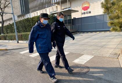 Hombres chinos con máscaras pasan por delante de la sede de la empresa estatal PetroChina en Pekín el 20 de enero de 2021