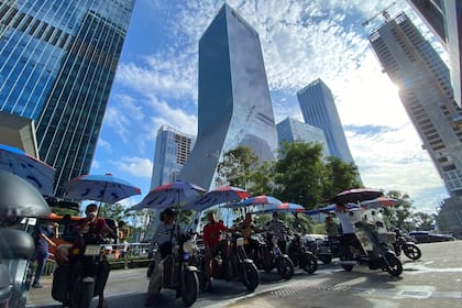 Hombres en bicicletas eléctricas esperan por pasajeros delante de las oficinas centrales del promotor inmobiliario Evergrande Group en Shenzhen, China, el 24 de septiembre del 2021. (AP Foto/Ng Han Guan)