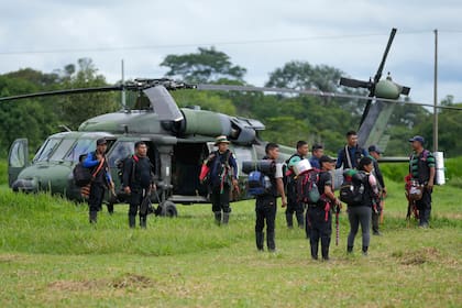 Hombres indígenas esperan para abordar un helicóptero en una base militar en Calamar, Colombia, el martes 23 de mayo de 2023, para ayudar en la búsqueda de cuatro niños desaparecidos después de un accidente aéreo