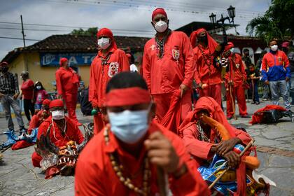 Hombres vestidos de rojo para representar "los demonios", usan barbijos protectores durante las celebraciones del Corpus Christi, en Yare
