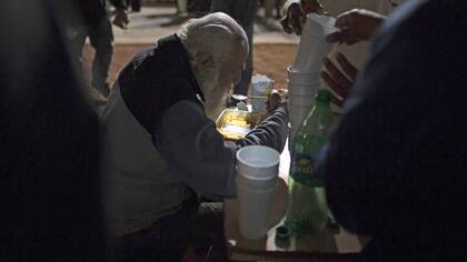 Un mendigo come en una olla popular frente al Congreso de Buenos Aires.