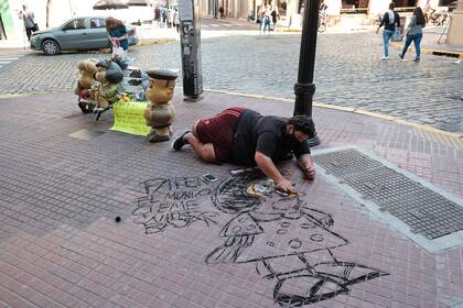 Homenajes y recuerdos de personas en las estatuas de Mafalda, Manolito y Susanita en Defensa al 700. En el piso Buda Tom hace un dibujo.