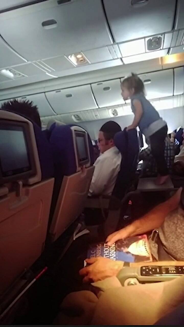 Niña no mayor de cuatro años de pie sobre la mesa plegable de uno de los asientos