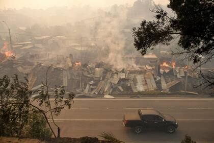 Humo y llamas se elevan desde las casas alcanzadas por el fuego durante los incendios forestales en Concepción, Chile, el 18 de enero de 2026