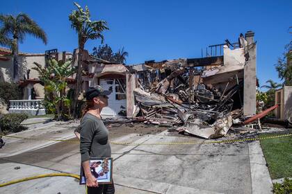 Lynn Morey se para frente a su casa quemada con un retrato de ella y su esposo, Keith Morey, recuperado por un bombero después de que las casas fueran destruidas por el Incendio costero en Laguna Niguel
