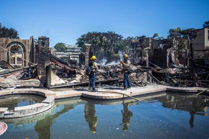 Los bomberos luchan contra los puntos críticos en una de las casas destruidas por el Incendio Costero en Laguna Niguel