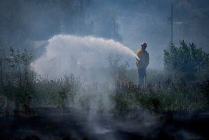 A firefighter directs water on a grass fire on an acreage behind a residential property in Kamloops, British Columbia, Monday, June 5, 2023. No structures were damaged but firefighters had to deal with extremely windy conditions while putting out the blaze. (Darryl Dyck/The Canadian Press via AP)