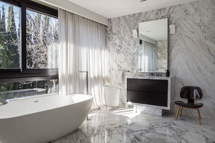 Íntegramente revestido en mármol (De Stefano), el baño de la suite se proyectó
con grandes aberturas que dejan pasar la luz natural. Silla Eames ‘Plywood’ (Un Lugar Así)