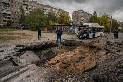 Investigadores examinan un cráter y un autobús dañado, tras un ataque con misiles en Dnipro el 10 de octubre de 2022, en medio de la invasión rusa de Ucrania.
