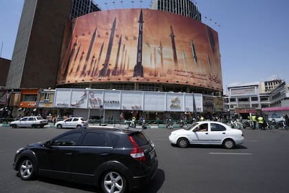 Los vehículos pasan junto a una pancarta antiisraelí que muestra el lanzamiento de misiles, en una plaza en el centro de Teherán, Irán, el viernes 19 de abril de 2024