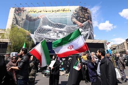 Iraníes sostienen banderas nacionales bajo una gran valla publicitaria que dice “El Estrecho de Ormuz permanece cerrado”, en Teherán, el 8 de abril de 2026