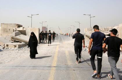 Iraquíes caminan a lo largo del puente afectado de Al-Jumhuriya que conduce a la Zona Verde de alta seguridad de Bagdad el 31 de julio de 2022, un día después de que los partidarios del clérigo iraquí Moqtada Sadr irrumpieran en el Parlamento dentro de la zona protegida