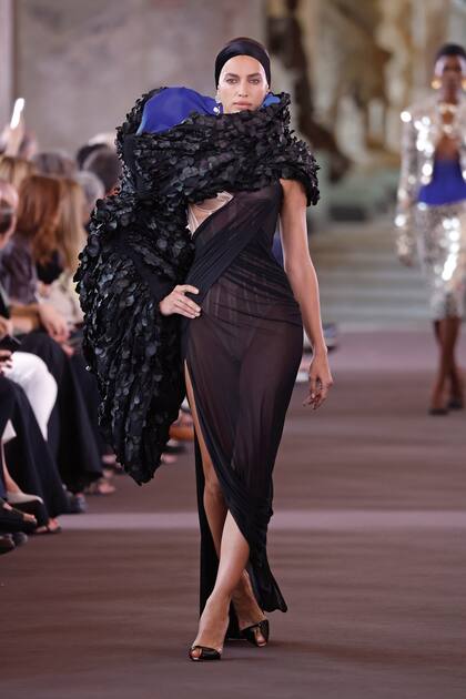 Irina Shaik con una capa con pétalos negros, forrada en azul Klein, sobre un corset velado por una transparencia.