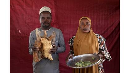 Isa Zakariya Audu sostiene pedazos de leña, mientras que Kakaye Ahmadu Maikifi sostiene un plato de okra
