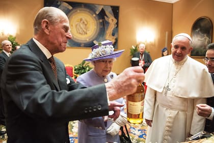 Isabel II y Felipe de Edimburgo le entregan regalos al papa Francisco durante su visita al Vaticano, en abril de 2014. La pareja real le llevó a Su Santidad una canasta con miel, jugos, carne y whisky.