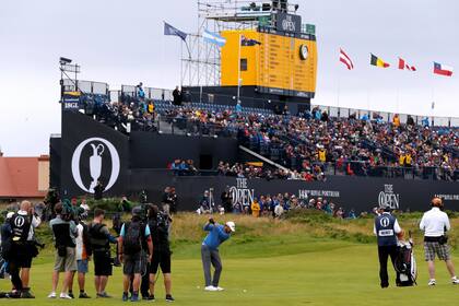 J. B. Holmes se apresta a golpear en el hoyo 18, con la atención de la prensa que genera un puntero; una bandera argentina flamea entre varias otras en la tribuna.