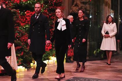 James Middleton, hermano de Kate, con su mujer,
Alizee Thevenet, con un equipo clásico y romántico compuesto por blazer
de terciopelo by Christie, con solapa y botonadura doble, y un pantalón
recto de la firma Emilio. Detrás, Pippa Middleton, con un elegante abrigovestido con hilos metalizados de la diseñadora Karen Millen. El clutch de
terciopelo y los stilettos, en rojo