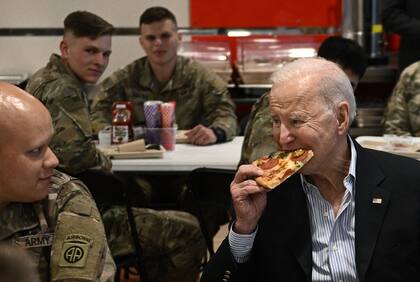 El Presidente de los Estados Unidos, Joe Biden, come una pizza mientras se reúne con miembros del servicio de la 82ª División Aerotransportada, que contribuyen junto a los aliados polacos a la disuasión en el flanco oriental de la Alianza, en la ciudad de Rzeszow, en el sureste de Polonia, el 25 de marzo de 2022. 