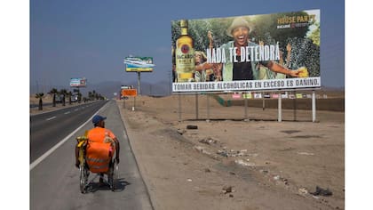 José Suárez, de Cúcuta, Colombia, mueve su silla de ruedas a lo largo de la Carretera Panamericana bordeada de carteles publicitarios de ron, lotería y nueces mixtas, al sur de Lima
