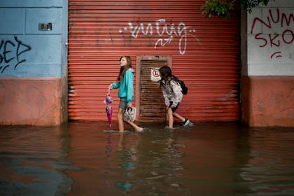 Jóvenes caminan por una calle inundada después de fuertes lluvias en Avellaneda, en las afueras de Buenos Aires, Argentina.