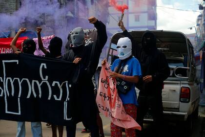 Jóvenes manifestantes gritan consignas y sostienen bengalas durante una protesta antigolpista en Yangon, Myanmar, el 25 de julio de 2022