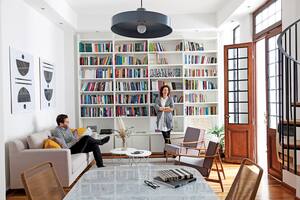 Joy y su marido en el living equipado con un amplio sofá (Loft) y dúo de sillones individuales heredados. La biblioteca (Melazza) es un diseño de Ideï. Los cuadros también son obra de ella.