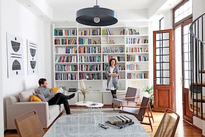 Joy y su marido en el living equipado con un amplio sofá (Loft) y sillones individuales heredados. La biblioteca (Melazza) es un diseño de Ideï Arquitectura.