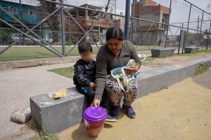 Juana junto a su hijo después de recibir un recipiente con comida en el comedor La Gargantita, en la villa Zavaleta, en Barracas