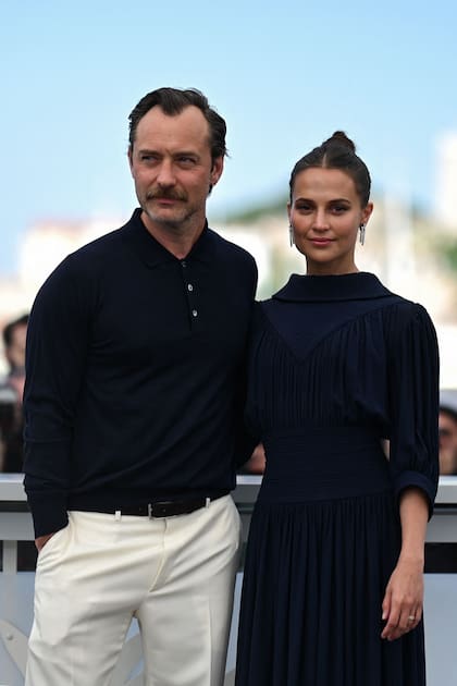 Jude Law y Alicia Vikander posando en uno de los eventos en el marco de la presentación de su nuevo film Firebrand en la edición 2023 del Festival de Cine de Cannes. Mientras él combinó una chomba azul con un pantalón de vestir blanco, ella eligió un vestido azul petróleo súper elegante