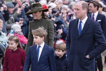 Kate y William guían a sus hijos. Adelante va el mayor de ellos, George, y le siguen Charlotte y Louis, con tapados iguales, pero en distinto color.