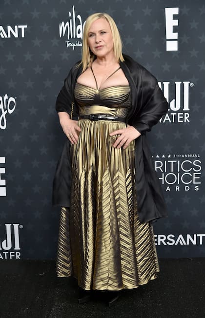 La actriz Patricia Arquette brilló con un vestido en dorado metalizado de falda plisada y cinturón que completó con una maxicapa de seda negra