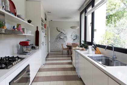 La amplia cocina, inundada de luz natural que entra por los ventanales. Atrás, el comedor diario. Los gallos pintados sobre la pared son obra de Manuela Durañona Art.