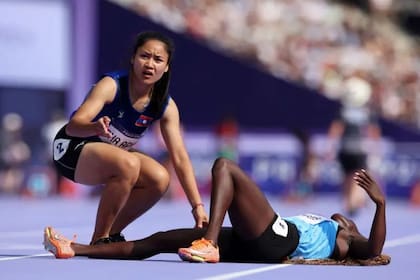 La atleta de Laos Pha Aphay atiende a su colega Lucia Moris de Sudán del Sur durante una carrera de clasificación para la prueba de 100 metros femenino.