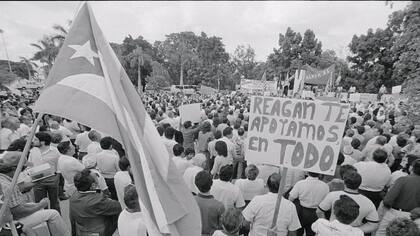 La bandera cubana ondea a la izquierda de un letrero que dice "Reagan, te apoyamos en todo" durante una manifestación de apoyo al presidente de EE.UU. en Miami en 1983.