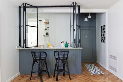 La barra está revestida con MDF ranurado que simula un machimbre. Se pintó con el gris azulado 8263 de Sinteplast, igual que la puerta de entrada y el techo del hall. División de hierro y vidrio repartido (Los Herreros de Vulcano) y banquetas tipo ‘Mar del Plata’.