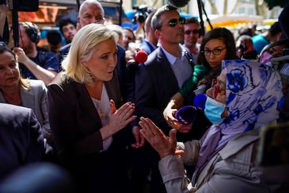 La candidata de extrema derecha Marine Le Pen habla con una mujer durante un acto de campaña en un mercado de Pertuis, Francia, el viernes 15 de abril de 2022. (AP Foto/Daniel Cole)