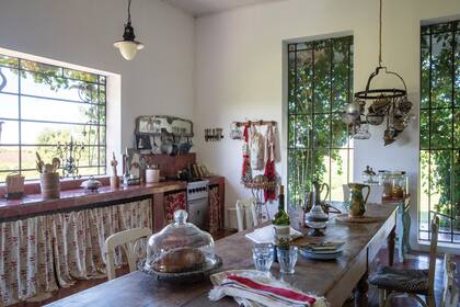 La cocina, con grandes ventanales y una mesa bien larga estilo campo. El estampado de los géneros, tipo toile de Jouy, también tiene animales.