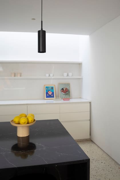 La cocina, discretísima y bicolor, de cerca. Isla revestida en mármol negro Marquina con terminación "leather" y muebles bajomesada de MDF con lustre poliuritánico blanco.
