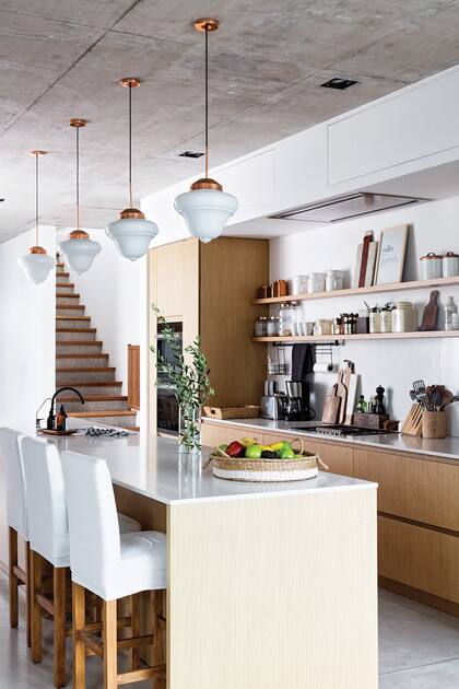 La cocina es de concepto abierto, con muebles enchapados en roble claro y mesada de silestone, donde se destacan las lámparas gota