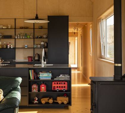 La cocina es negra y contrasta con la la madera clara y la luz natural que invade los ambientes