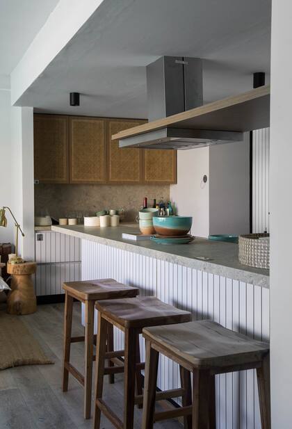 La cocina integrada al living permite cocinar mirando al agua. Mesada en Purastone 'Coralina' (De Stefano). Revestimiento ranurado 'Everest' de la línea 'Étnica' (FaPlac). Banquetas (Wood Market). Vajilla (Barro Alfarería).