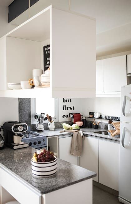 La cocina integrada es súper funcional y la usan mucho. Cuando Lara y Franco están solos, comen en la barra porque les resulta más cómodo, al tener todo al alcance. El toque de diseño lo dan la vajilla en negro, bol y jarra de cerámica rayados (Blanc Buenos Aires) y el vinilo en la pared “But First