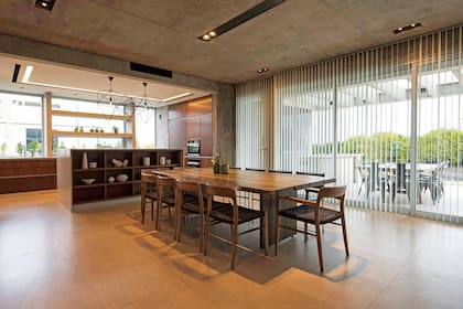 Mesa de palo santo (Palo Santo Maderas) y sillas ‘Moller’ de lenga (Navarro Hábitat). La abertura de seis hojas en aluminio anodizado con DVH tiene cortinas con bandas